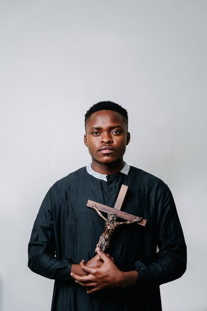 Portrait of a young man in a cassock holding a crucifix, symbolizing faith and Christianity.