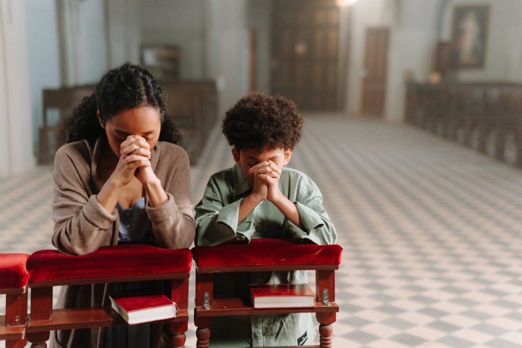 A mother and son kneeling and praying together inside a serene church.