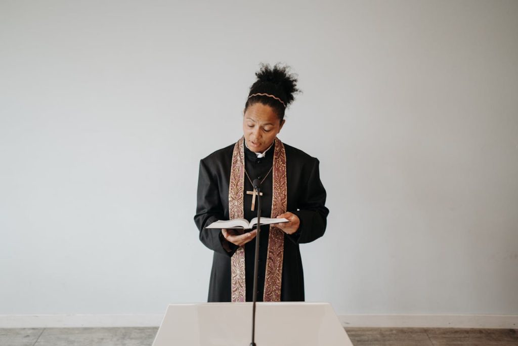 A female priest in a cassock reading the Bible during a church service, conveying a serene religious atmosphere.